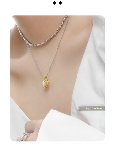Close-up of layered necklace with golden heart pendant and silver beaded chain on model