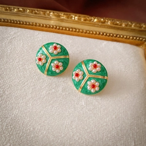 Vintage round earrings with green enamel and pearl floral patterns on beige fabric