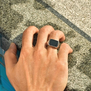 Macro shot of silver men's signet ring with black rectangular stone on wet skin