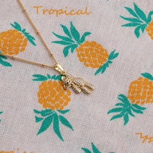 Collier avec pendentif ourson doré et cristaux scintillants sur fond d'été tropical
