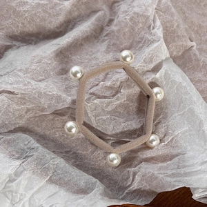 Detailed view of beige elastic hair tie with six elegant white pearls on textured paper