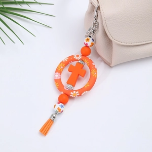 Detail of orange silicone cross keychain with decorative beads, tassel and floral patterns