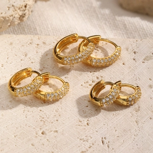 Three sizes of gold-plated hoop earrings with pave diamonds on a stone background