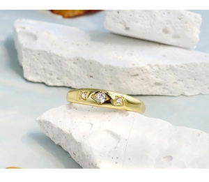 Macro detail of gold ring featuring three round gemstones set on a white stone texture