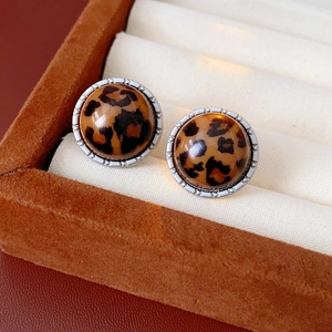 Détail de boucles d'oreilles rondes à motif léopard dans un écrin en velours brun