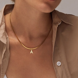Close-up of a gold snake chain necklace with a sparkling zircon letter A pendant on a model