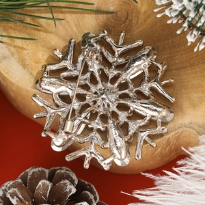 Detailed back view of silver snowflake brooch with pin clasp on wooden base with pine cones