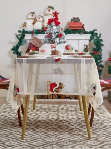 Detail of festive beige lace tablecloth with embroidered Santa hats and snowman motifs