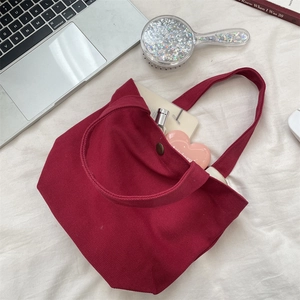 Close-up of burgundy canvas tote bag featuring vintage metal button closure and spacious interior