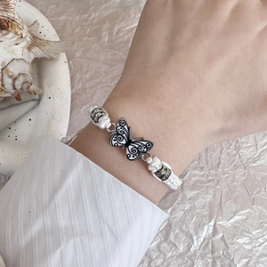 Close-up of a white woven bracelet featuring a black and white butterfly pendant and beads