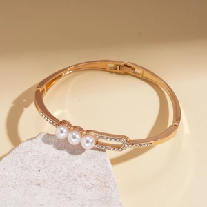 Elegant gold-plated bangle featuring three center pearls and sparkling crystals on a stone base