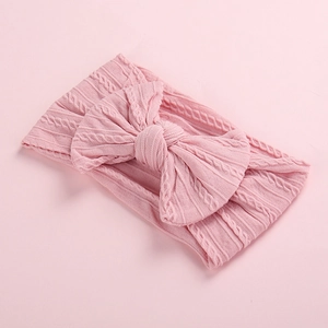 Detail shot of pink knitted baby headband with large bow and cable knit texture