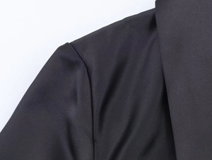 Detailed close-up of glossy black satin fabric and fine stitching on the shoulder seam