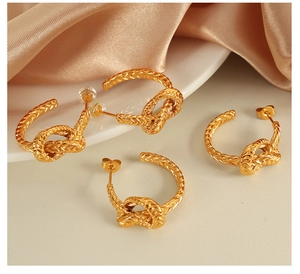 Gros plan de boucles d'oreilles nœuds dorées sur soie champagne et plateau de céramique