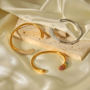 Close-up of gold and silver open bangles with pearls and crystals on satin fabric