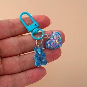 Close-up of blue gummy bear and glitter heart charm on light blue lobster clasp