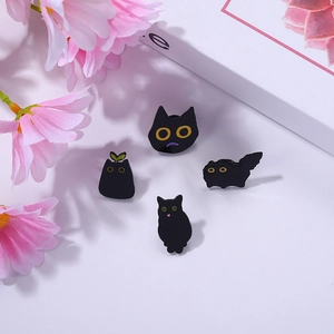 Detailed view of four cute black cat enamel pins set against a floral background