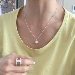 Close-up of a 925 silver beaded necklace with heart pendant and wide H-shaped ring