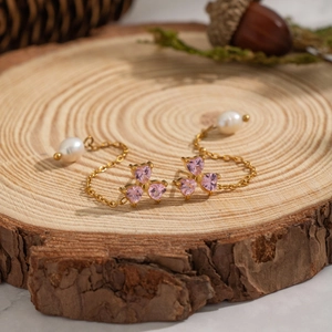 Golden chain earrings with pink heart gemstones and white pearl on natural wood