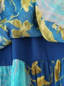 Detailed close-up of blue chiffon fabric with yellow floral prints and tiered pleats