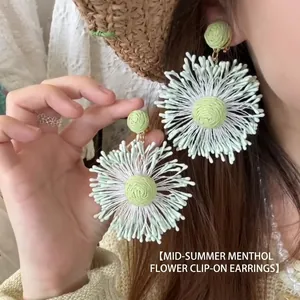 Macro view of hand-woven mint green and beige floral earrings with textured fibers