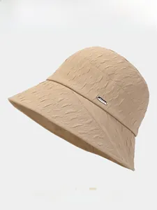 Detailed close-up of khaki bucket hat showing textured fabric and silver metal plaque