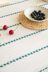 Detailed blue leaf embroidery on a beige linen table runner with a rustic home setting