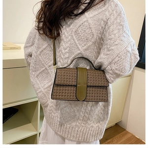 Detail of woven texture dark brown crossbody bag with green flap strap and shoulder strap