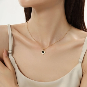 Close-up of heart-shaped black enamel pendant with radiant gold edge on female model