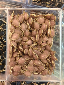 Bulk pink teardrop semi-precious stone pendants with gold metal edging in storage box