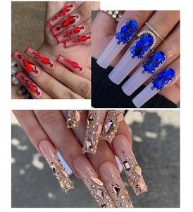 Close-up of long false nails featuring red, blue, and champagne flatback crystal designs