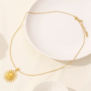 Collana minimalista con pendente a sole dorato su vassoio in ceramica bianca
