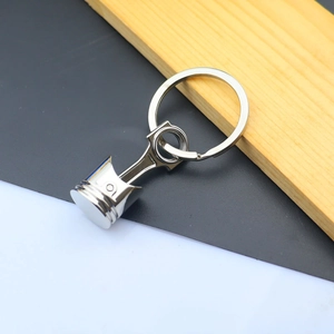 Polished metal piston keychain detail with circular keyring against a wood background