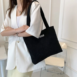 Detail view of the black corduroy tote bag featuring a white 'FASHION' label and ribbed texture