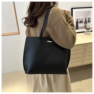Close-up of minimalist black leather tote bag worn by a model in a cozy interior setting