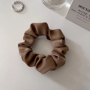 Close-up of a brown satin silk scrunchie with soft folds and elegant glossy texture