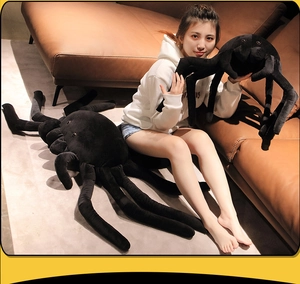 Size comparison of plush black spider toys with small and giant models on sofa