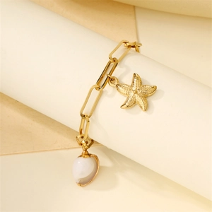 Close-up of golden shell and starfish charms on a stainless steel beach bracelet