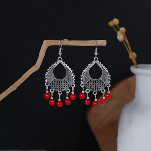 Detail of vintage bohemian silver teardrop earrings with red beaded tassels on wood