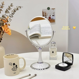 Detail of an oval desktop makeup mirror with a white frame and adjustable chrome stand