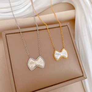 Elegant gold and silver bow necklaces with white shell inlay on a beige jewelry box