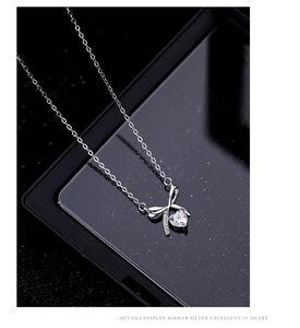 Macro shot of silver bow heart pendant with sparkling cubic zirconia on a reflective surface