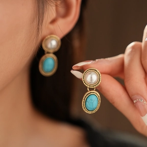 Close-up of vintage gold finish earrings with faux pearl and turquoise gemstone inlay