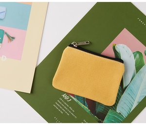 Flat lay of a yellow canvas coin purse with silver zipper on a tropical magazine background