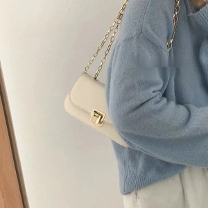 Minimalist cream shoulder bag with gold chain strap worn by a model in casual attire
