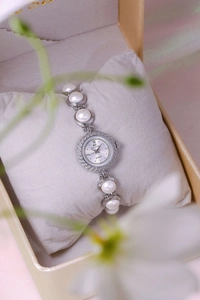 Close-up of silver pearl bracelet watch with rhinestone dial on a soft cushion