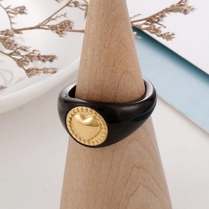 Close-up of black resin ring with a golden heart medallion on a wooden jewelry display