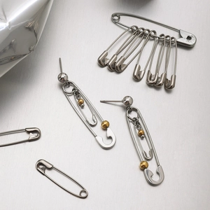 Detail of silver safety pin earrings with gold bead accents on a textured metallic surface