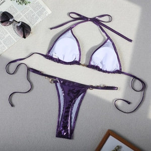 Flat lay of purple metallic bikini set with tie-side thong and ring details on grey texture