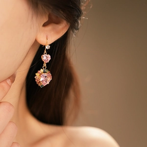 Detailed close-up of golden heart earrings with pink stones and colorful zircon accents